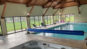 Una piscina interior con jacuzzi, ventanas amplias y vista a un área verde.