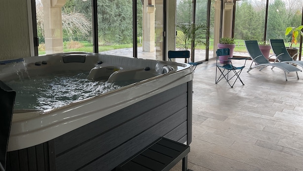 Un jacuzzi en una habitación amplia con ventanas grandes, mobiliario exterior y plantas en macetas.