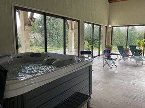 A hot tub in a spacious room with large windows, outdoor seating, and potted plants. - Ma Tranquillité (Courpière)