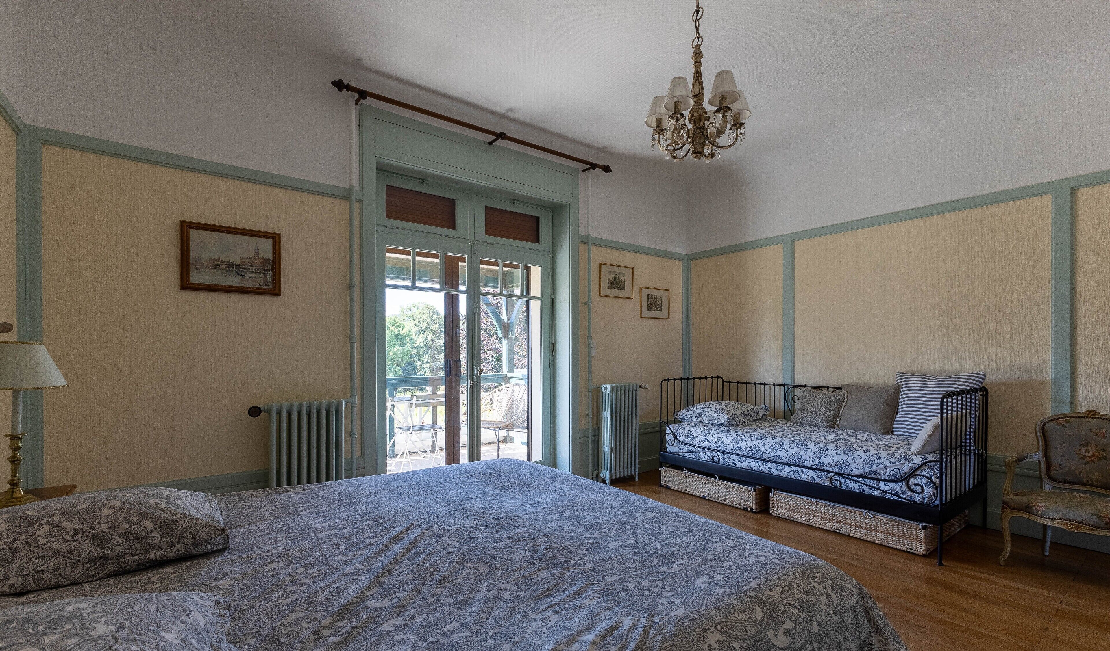 A bedroom with a bed, a sofa bed, a chair, a radiator, and a chandelier.