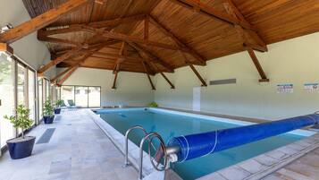 An indoor swimming pool with a wooden ceiling, clear glass walls, and a tiled floor.