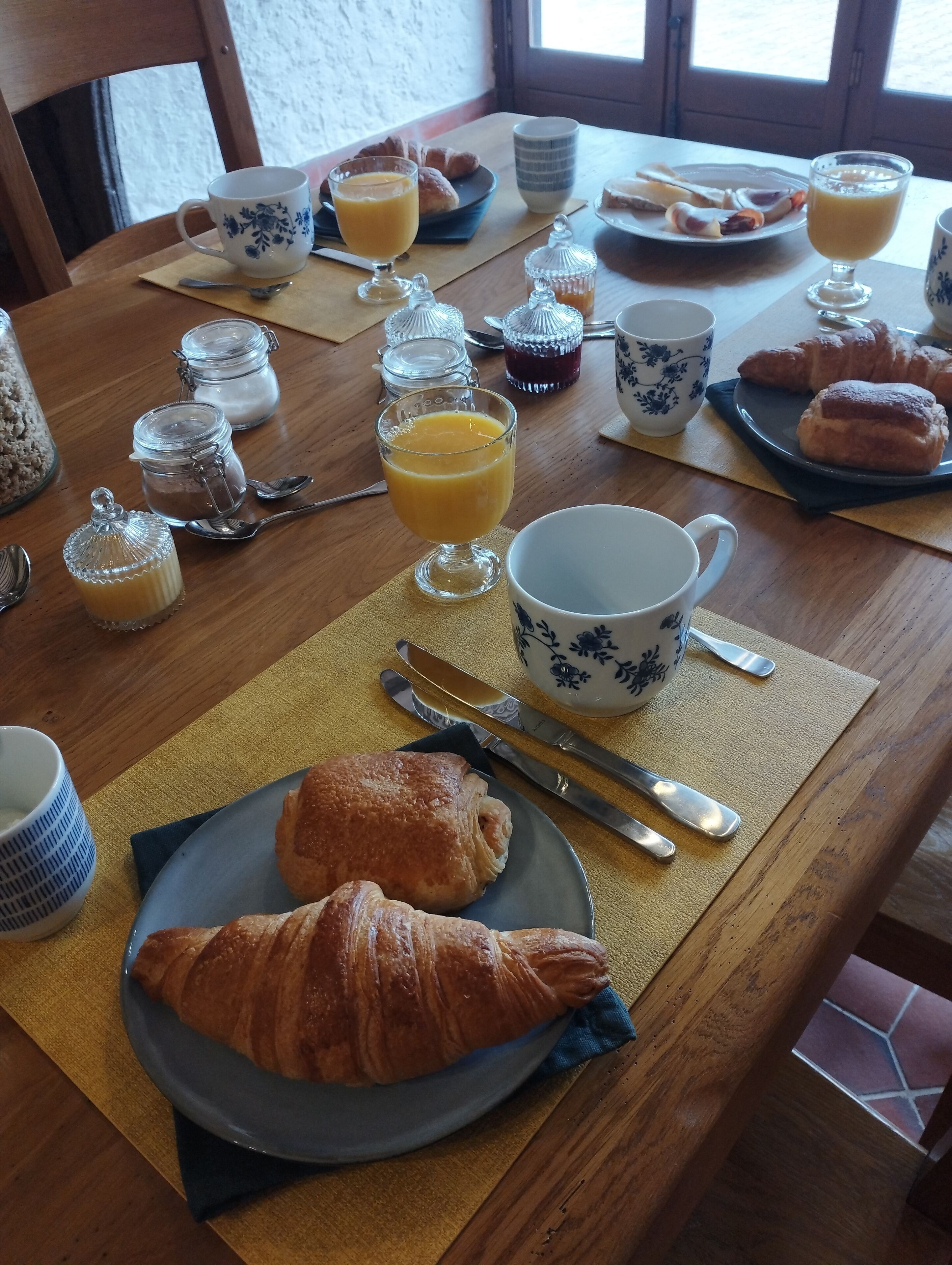A breakfast table with croissants, orange juice, and various condiments.