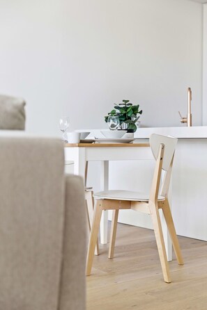 Moderni keittiö, jossa on ruokapöytä, tuoleja ja ruukkukasvi.