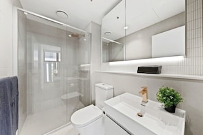 Ein modernes Badezimmer mit Duschkabine aus Glas, einer weißen Toilette, einem Waschbecken mit goldfarbenem Wasserhahn und einem Topf mit Pflanze.