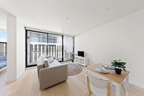 Ein modernes Wohnzimmer mit einer Couch, einem Esstisch mit Stühlen, einem Fernseher und einem Balkon mit Blick auf Gebäude.