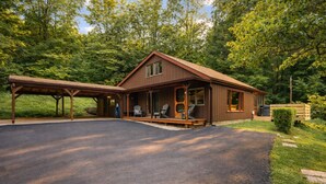 A two-story wooden cabin with a covered porch, a driveway, and a well-maintained lawn. - Lakefront in Logan (In the heart of Hocking Hills) (Logan)