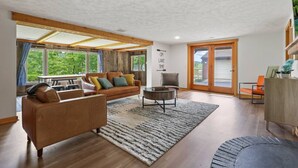 A spacious living room with a large window, a sofa, a coffee table, and a wooden cabinet. - Lakefront in Logan (In the heart of Hocking Hills) (Logan)