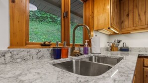 A kitchen with a large sink, wooden cabinets, and a window overlooking greenery. - Lakefront in Logan (In the heart of Hocking Hills) (Logan)