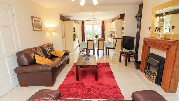 Een woonkamer met een bruine leren bank, een rood vloerkleed, een televisie en een open haard.