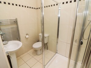 Un baño con ducha de mampara de vidrio, inodoro y lavamanos.