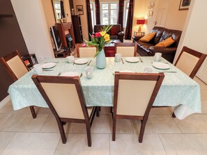 Un comedor con una mesa dispuesta para cuatro personas, sillas, un jarrón con flores y un sofá al fondo.