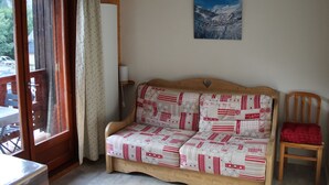 A cozy room with a wooden sofa, a red chair, a window with curtains, and a painting on the wall. - Studio for 4, balcony, shared parking (Valloire)