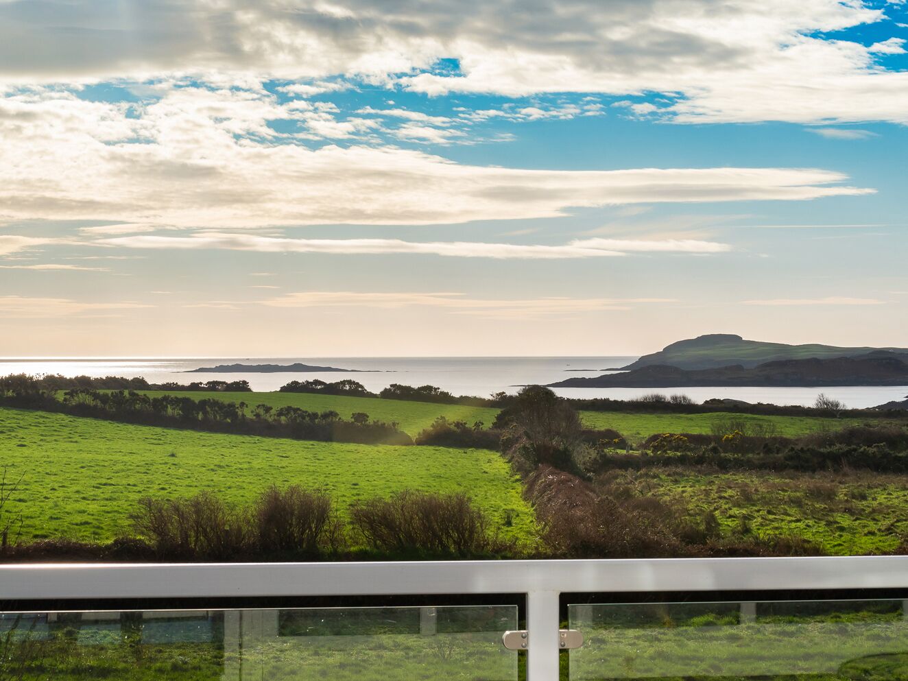 A coastal landscape with green fields, a body of water, and distant hills.