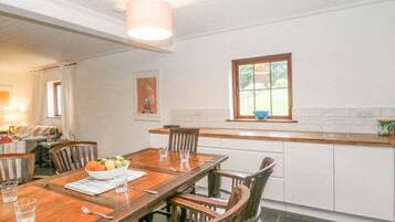 A dining area with a wooden table, chairs, and a bowl of fruit. There is a window with a view of greenery outside.