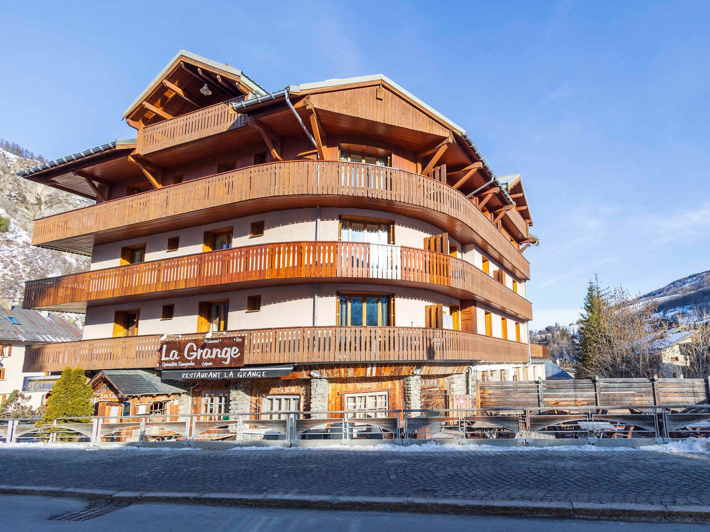 A multi-story wooden building with balconies, a sign reading 'La Grange Restaurant La Grange,' and a mountainous backdrop.