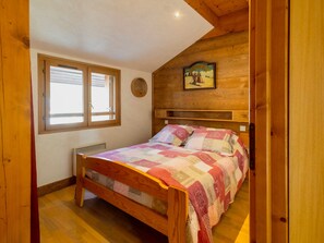 A bedroom with a wooden bed, a window, and a wall-mounted picture. - Spacious Comfort for 12 with Mezzanines in Valloire (Valloire)