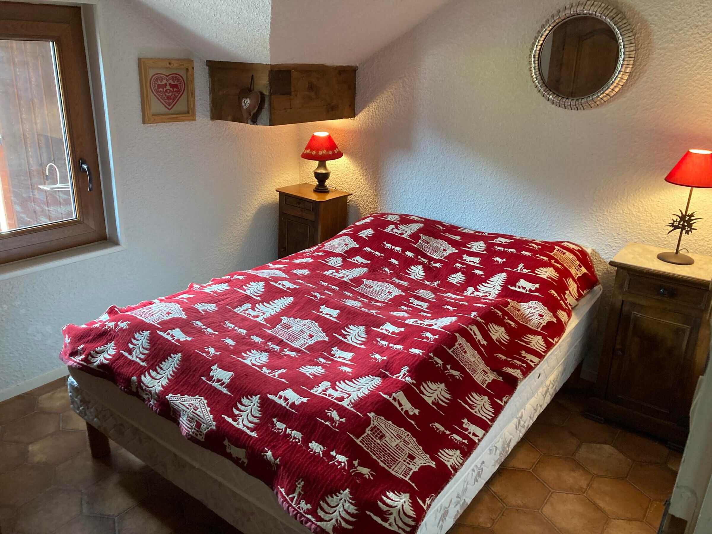 Ein Schlafzimmer mit einem Bett, zwei Nachttischen, einem Fenster und einem Spiegel an der Wand.