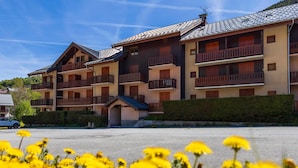 A multi-story hotel with balconies, a parking lot, and yellow flowers in the foreground.