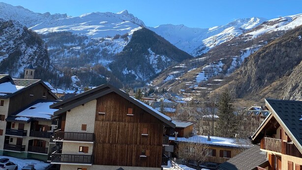 A mountain village with wooden buildings, a church, and snow-covered peaks in the background.