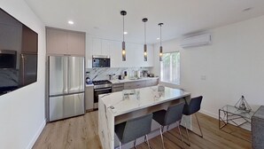 A modern kitchen with a central island, stainless steel appliances, pendant lighting, and a window providing natural light.