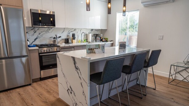 A modern kitchen with a marble island, stainless steel appliances, and bar stools.