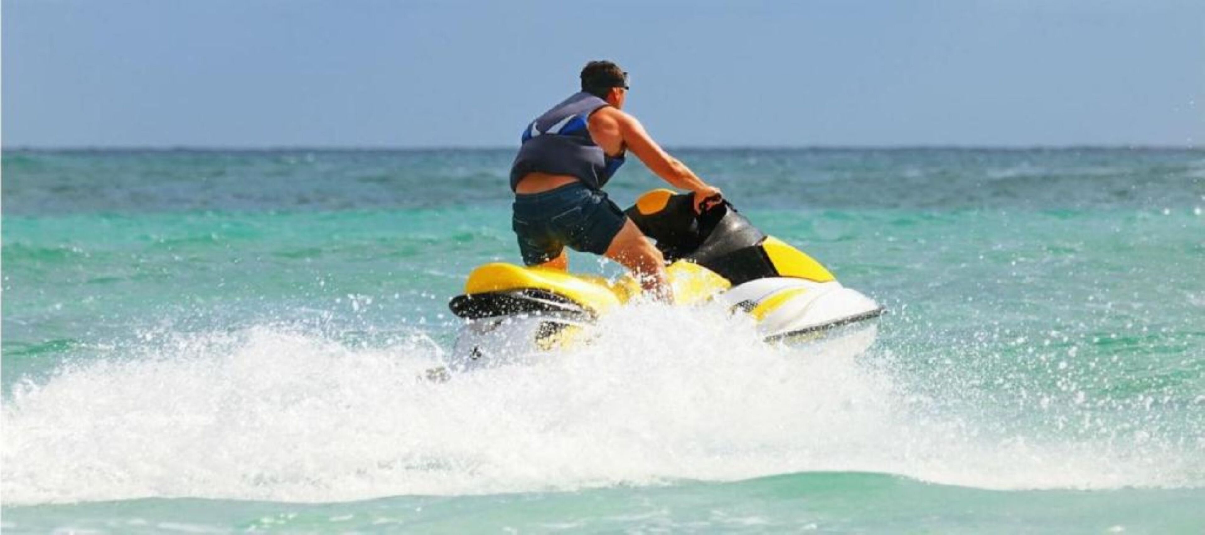 A person riding a yellow and black jet ski on clear turquoise water.