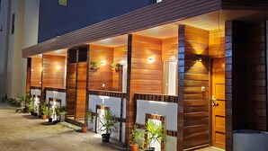 A row of wooden cabins with exterior lighting, potted plants, and a concrete pathway. - Batuta Maldives Inn (Thulusdhoo Island)