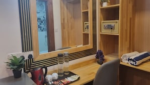 A hotel room with a large mirror, wooden shelves, a desk with a tray of toiletries, a red kettle, and a small plant. - Batuta Maldives Inn (Thulusdhoo Island)