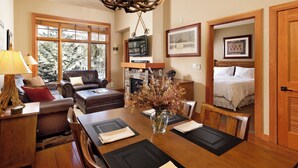 A spacious living room with a fireplace, a dining area with a large wooden table, and a bedroom with a bed and a door. - Glacier Cove | Capitol Peak Lodge #3125 | 1B/1B (Snowmass Village)