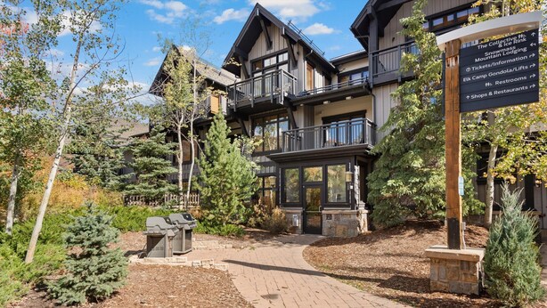 A lodge with a central entrance, multiple balconies, and a signpost with directional information. - Glacier Cove | Capitol Peak Lodge #3125 | 1B/1B (Snowmass Village)