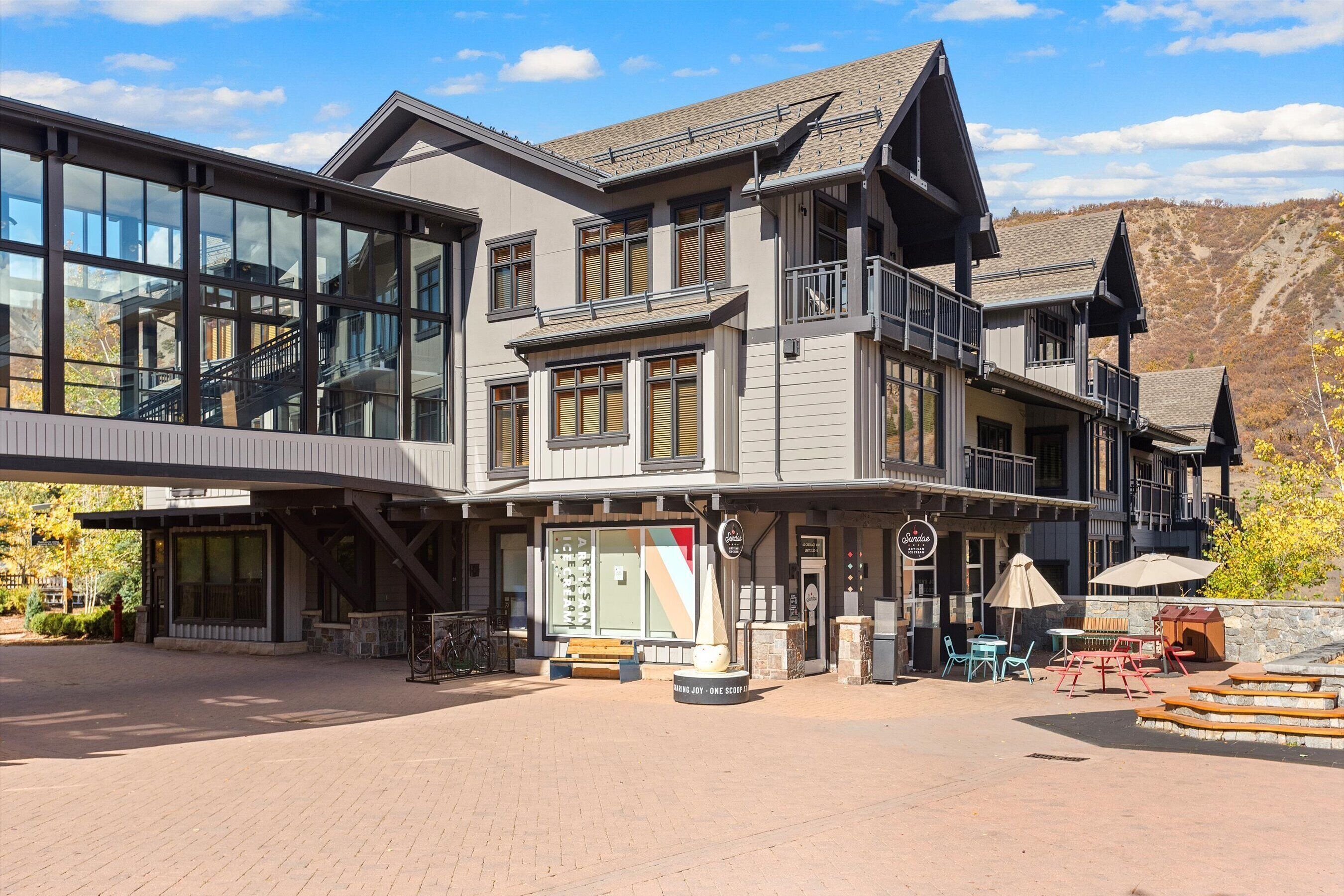 A multi-story building with large windows, a covered entrance, outdoor seating, and a mountain backdrop.