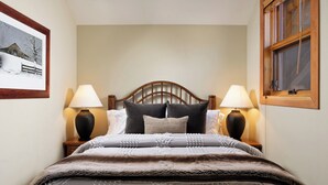 Een net opgemaakt bed met een houten hoofdbord, twee bedlampen en een ingelijst foto aan de muur.
