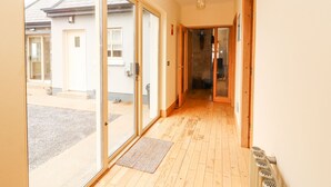 A hallway with glass doors leading to a courtyard, wooden flooring, and a small rug at the entrance. - Cúnna Bán (Fanore)