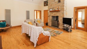 A spacious living room with a stone fireplace, wooden flooring, and a cozy seating area with a sofa and armchairs. - Cúnna Bán (Fanore)