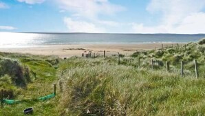 A beach with a grassy foreground and a clear sky. - Cúnna Bán (Fanore)