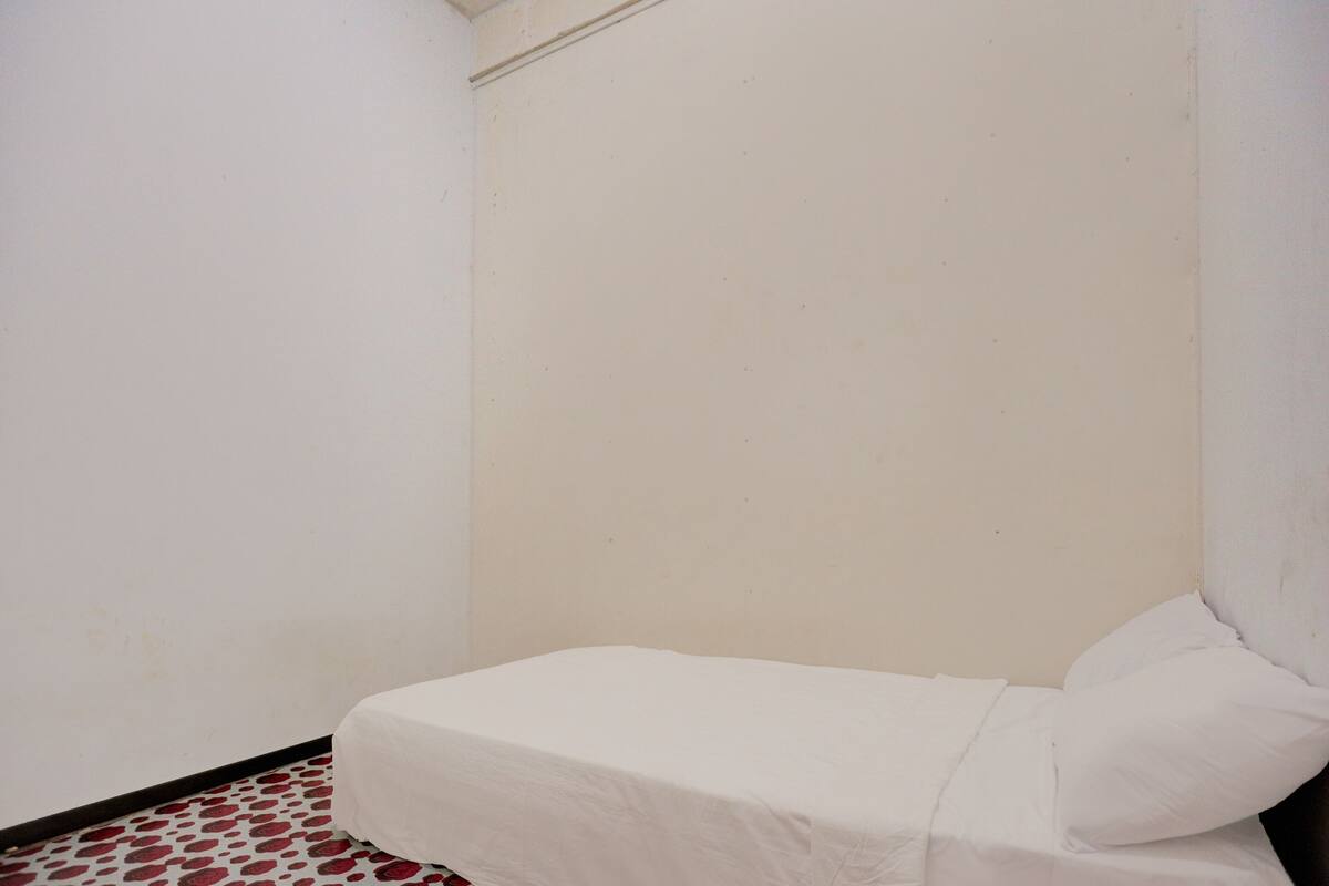 A small, single-bed room with a plain white wall and a patterned floor.