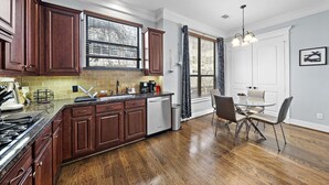 A modern kitchen with wooden cabinets, a stainless steel range, and a dining area with a glass table and chairs. - Near Heights, DT, Montrose, Washington | BBQ WiFi (Houston)