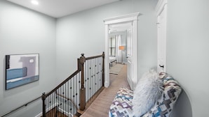A hallway with a staircase, a patterned bench, a framed artwork, and a door leading to another room. - Near Heights, DT, Montrose, Washington | BBQ WiFi (Houston)