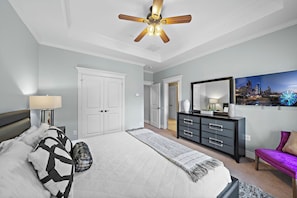 Ein Schlafzimmer mit einem Bett, einem Deckenventilator, einer Kommode, einem Spiegel und einem Stadtbild an der Wand.