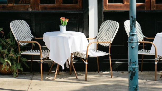 An outdoor seating area with two tables and four chairs, a vase with flowers, and a blue pole.