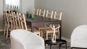A dining area with a dark wooden table surrounded by wooden chairs, a small black side table with a sculpture, and a green cactus on the table.