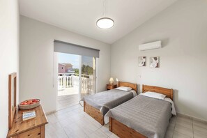 Un dormitorio con dos camas, una mesita de noche de madera, una cesta de fruta y vistas al balcón exterior.