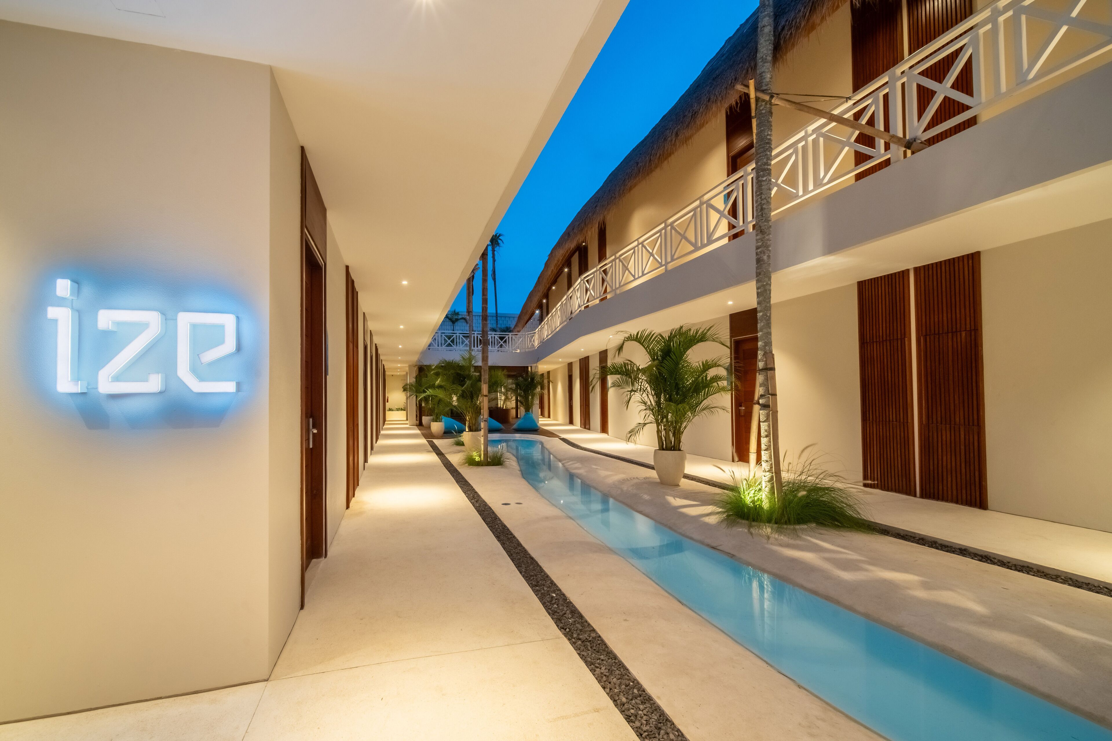 A hotel corridor with a pool, a neon sign, and a balcony with a railing.
