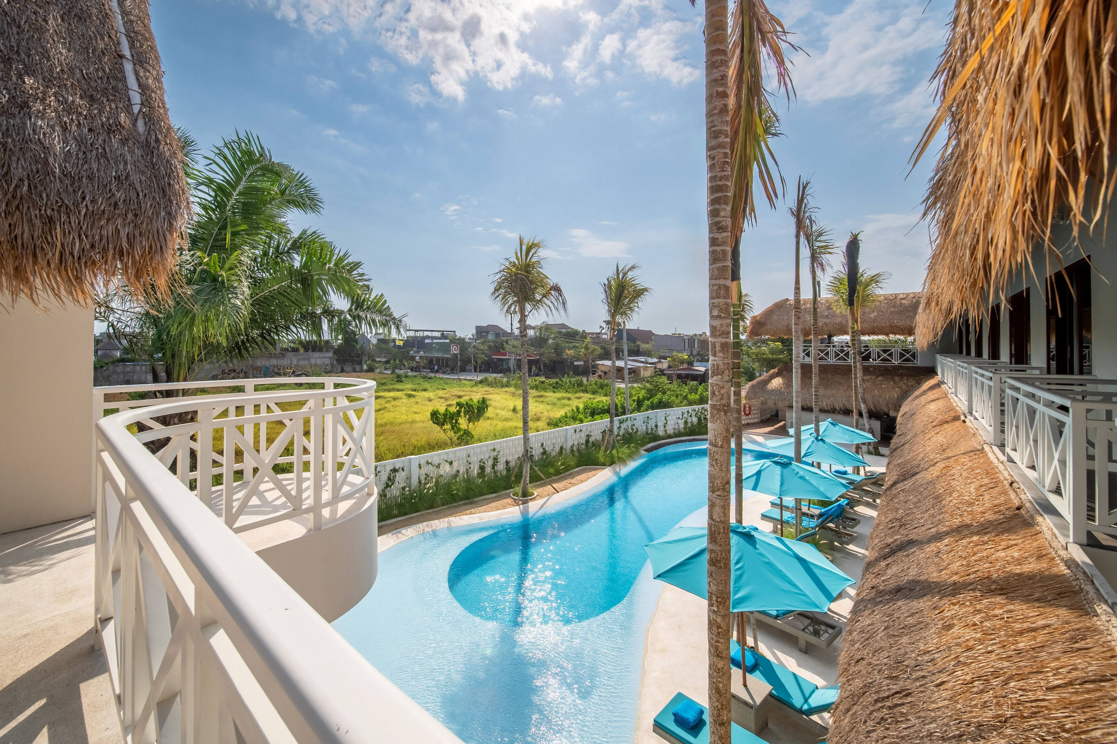 A pool area with a thatched roof, palm trees, and a view of the surrounding landscape.
