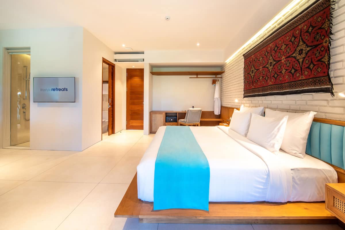 Una habitación de hotel moderna con una cama grande, un televisor y un tapiz rojo con motivos.