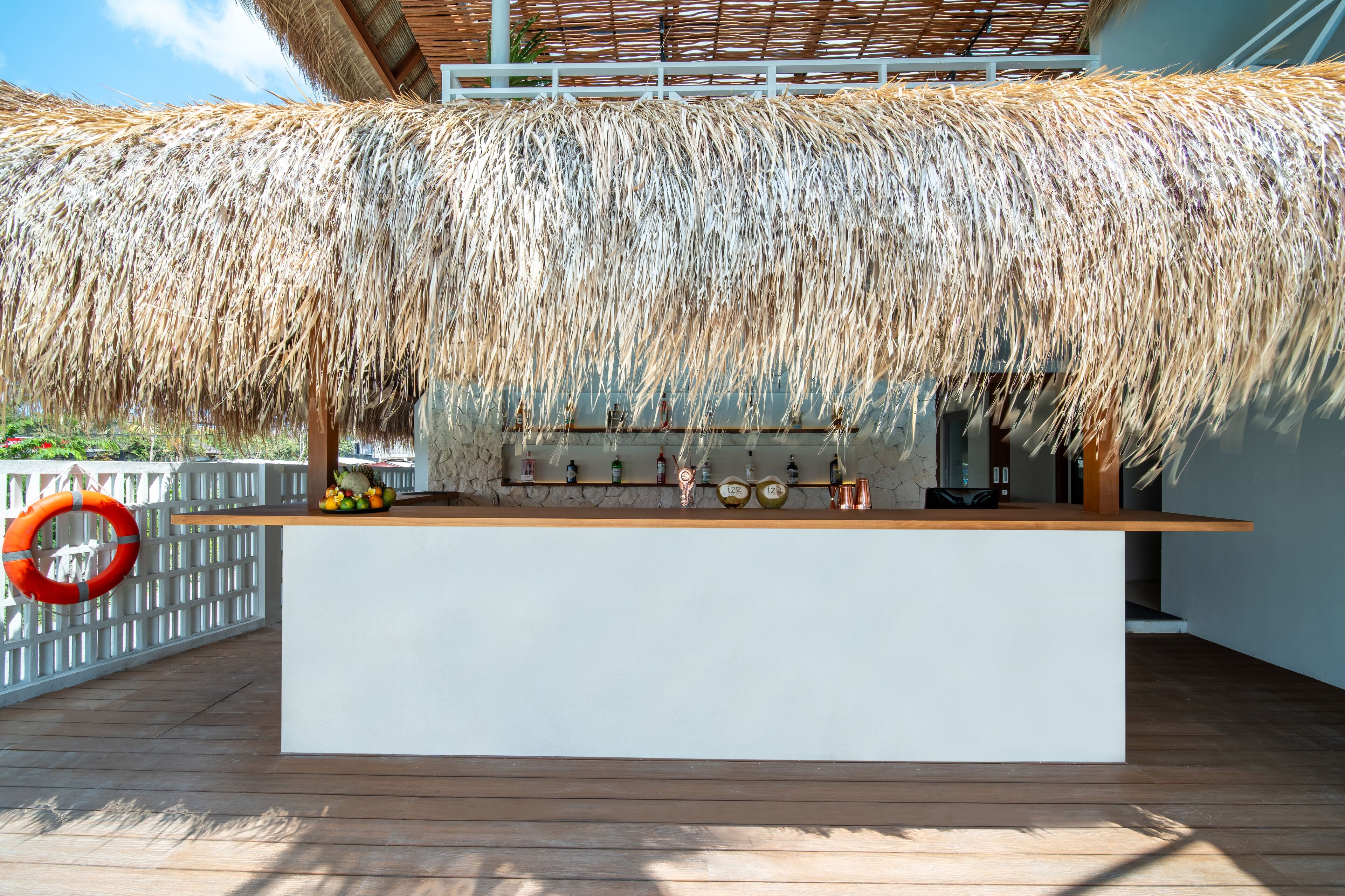 Un espace bar doté d’un toit de chaume, d’un comptoir blanc et de diverses bouteilles et verres.