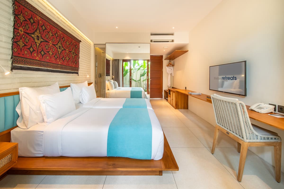 Habitación de hotel con dos camas, televisión, escritorio y baño a la vista.