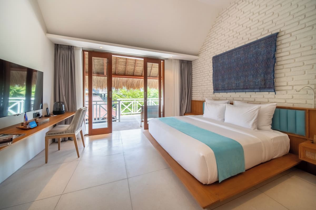 Habitación de hotel moderna con una cama grande, un escritorio con computadora y un balcón con vistas a zonas verdes.