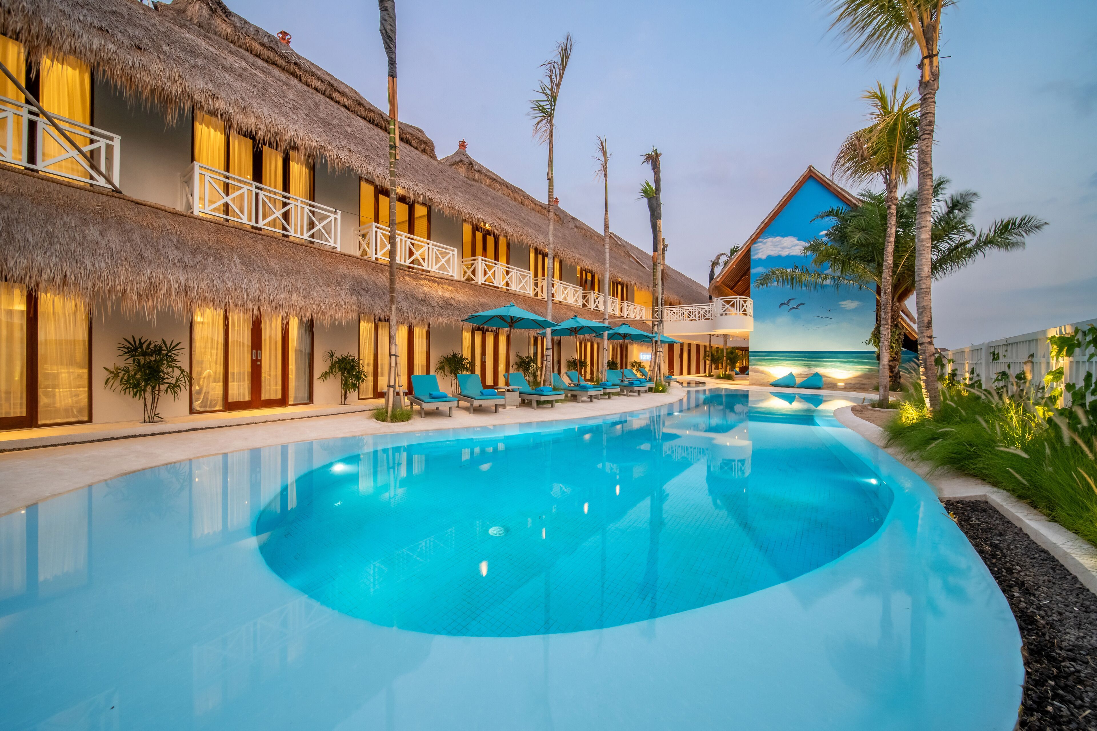 A resort with a swimming pool, thatched-roof buildings, and a mural of a beach scene.