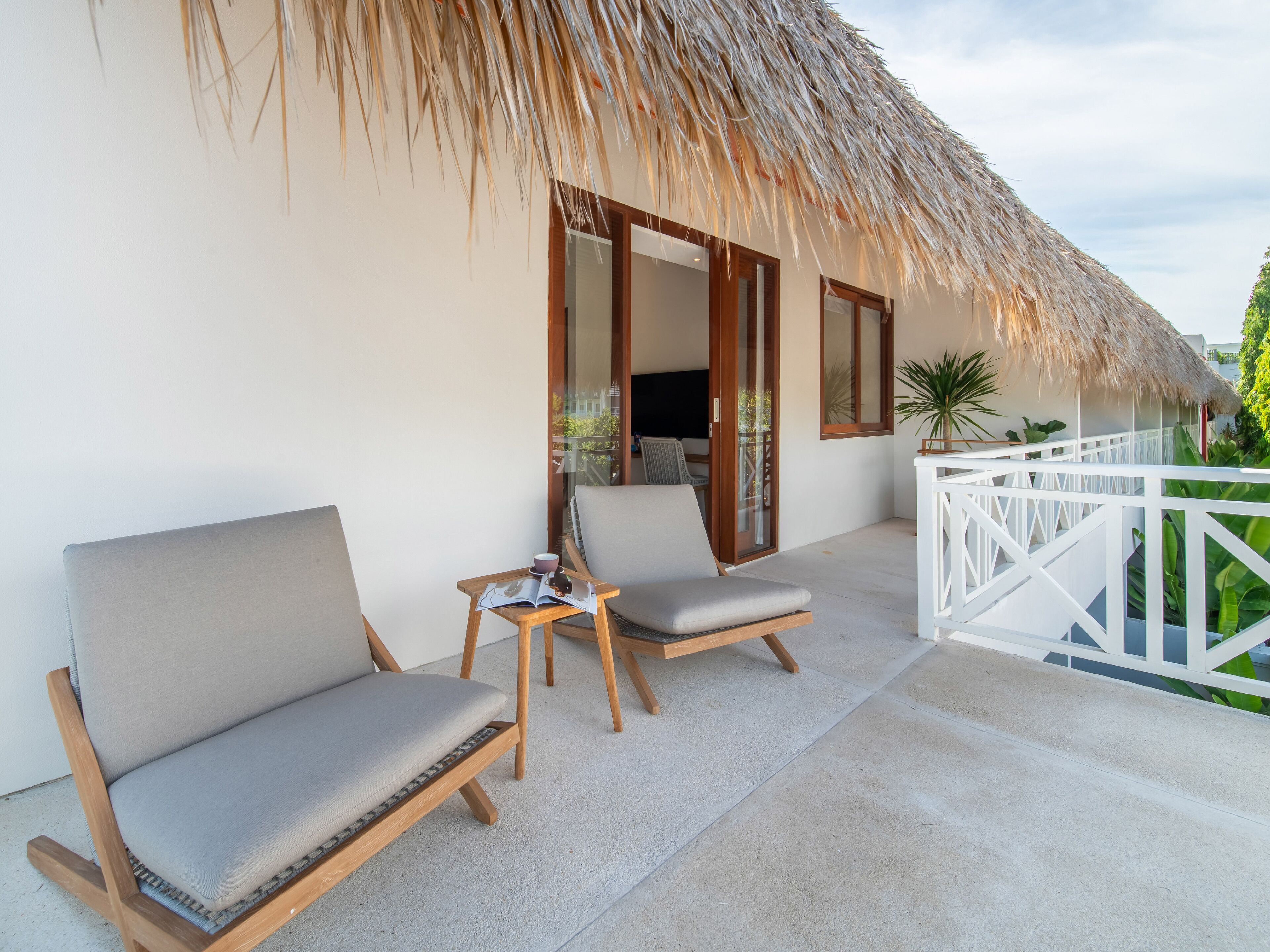 Un balcon avec deux fauteuils rembourrés et une petite table, un toit de chaume et une balustrade blanche.